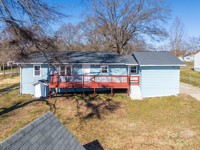 back of house featuring a shingled roof, a lawn, and a wooden deck