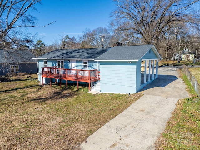 view of front facade featuring driveway, a front lawn, a deck, and roof with shingles