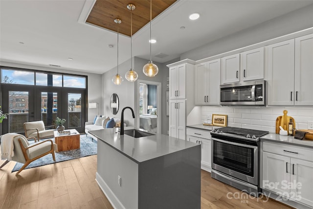 kitchen with appliances with stainless steel finishes, open floor plan, a sink, light wood-type flooring, and backsplash