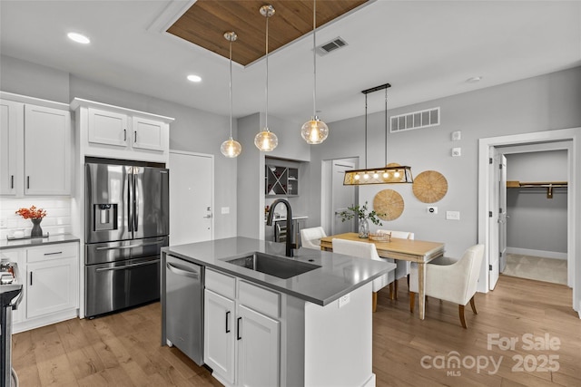 kitchen featuring stainless steel appliances, dark countertops, visible vents, and a sink