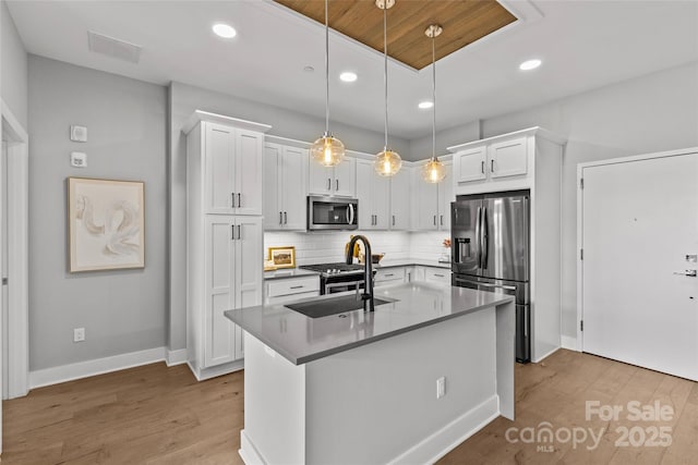 kitchen featuring tasteful backsplash, appliances with stainless steel finishes, white cabinetry, a sink, and wood finished floors