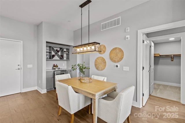 dining room featuring a bar, baseboards, visible vents, and wood finished floors