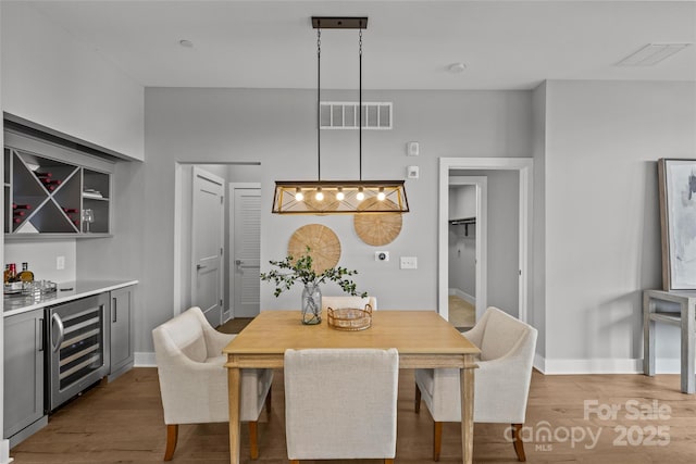 dining area featuring a bar, beverage cooler, visible vents, and wood finished floors