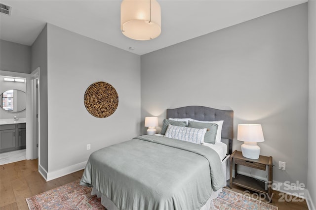 bedroom featuring visible vents, baseboards, ensuite bath, wood finished floors, and a sink