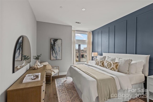 bedroom with visible vents, a decorative wall, and wood finished floors