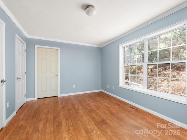 spare room featuring ornamental molding, visible vents, baseboards, and wood finished floors