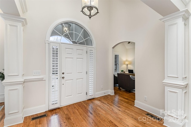 foyer featuring arched walkways, visible vents, decorative columns, and light wood finished floors