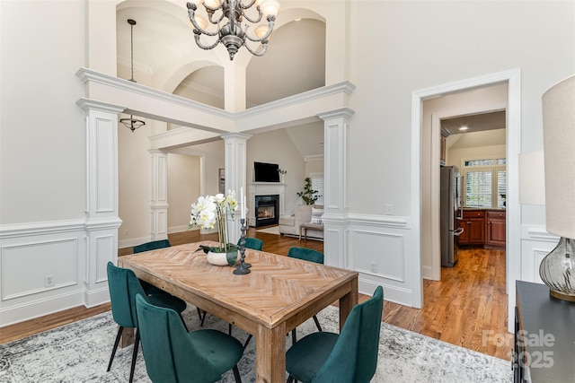 dining space featuring a chandelier, light wood-type flooring, a glass covered fireplace, and decorative columns