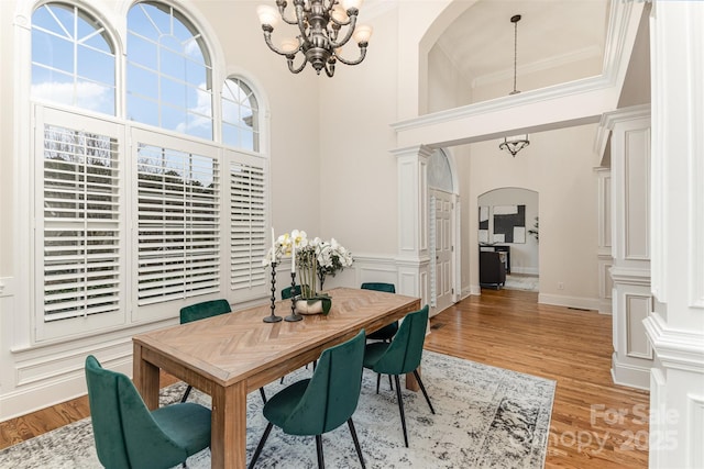 dining area featuring arched walkways, a towering ceiling, ornamental molding, light wood-style floors, and a chandelier