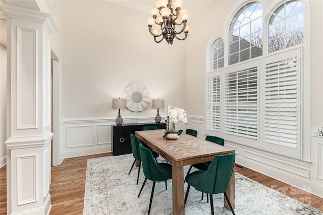 dining area with light wood finished floors, wainscoting, an inviting chandelier, crown molding, and a decorative wall