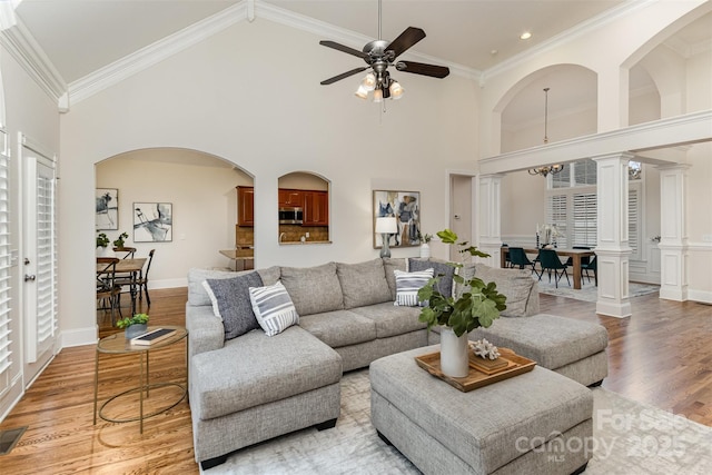 living room featuring light wood-type flooring, high vaulted ceiling, ornamental molding, and ornate columns