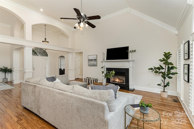 living room featuring high vaulted ceiling, a glass covered fireplace, crown molding, and wood finished floors