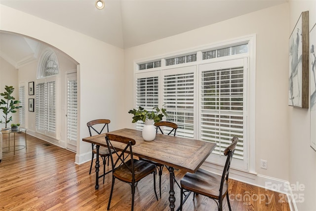 dining room featuring baseboards, arched walkways, vaulted ceiling, and wood finished floors