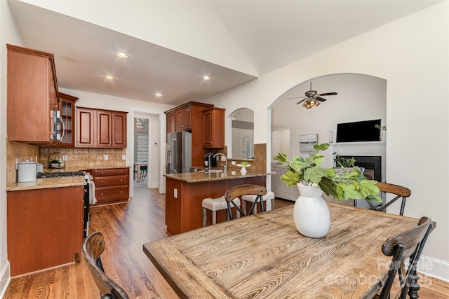 dining room with arched walkways, a fireplace, lofted ceiling, a ceiling fan, and dark wood-type flooring