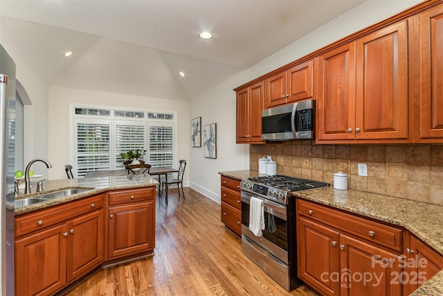 kitchen with light wood finished floors, backsplash, appliances with stainless steel finishes, vaulted ceiling, and a sink