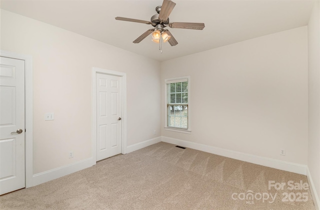 carpeted empty room with visible vents, a ceiling fan, and baseboards