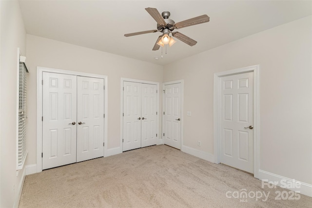 unfurnished bedroom featuring a ceiling fan, carpet flooring, baseboards, and two closets