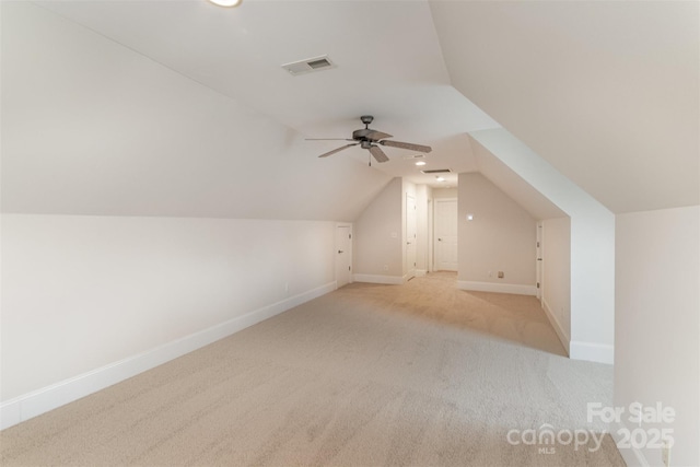 additional living space with light colored carpet, a ceiling fan, visible vents, vaulted ceiling, and baseboards