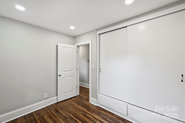 unfurnished bedroom featuring a closet, baseboards, dark wood-style flooring, and recessed lighting