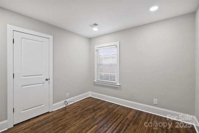 empty room with dark wood-style floors, recessed lighting, visible vents, and baseboards