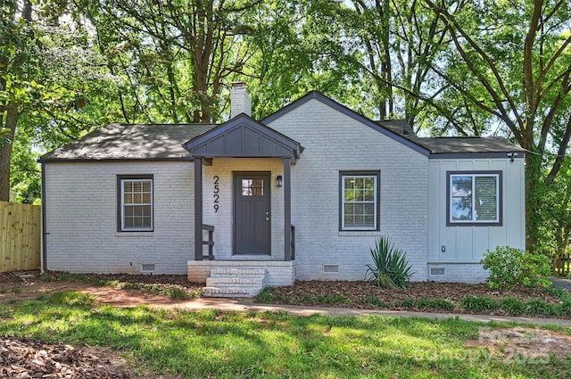 bungalow-style home featuring brick siding, fence, roof with shingles, crawl space, and a chimney