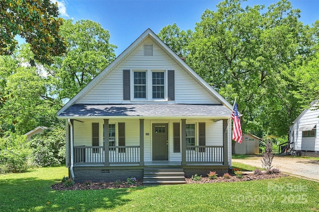 bungalow featuring covered porch, roof with shingles, and a front yard