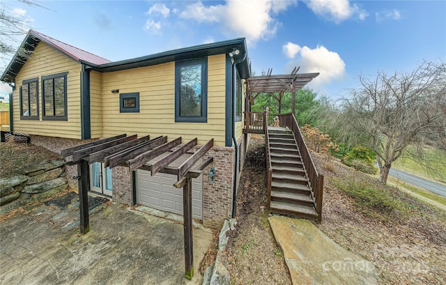 view of side of property with metal roof, an attached garage, brick siding, stairway, and a pergola