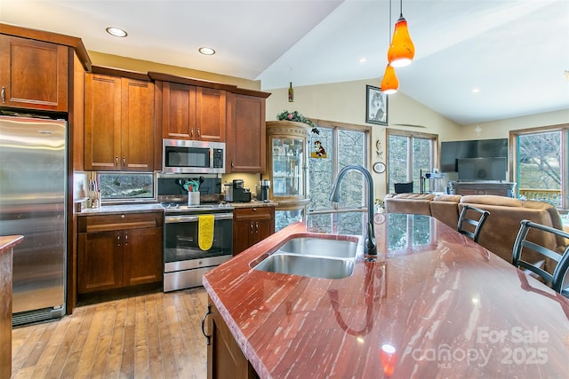 kitchen featuring lofted ceiling, hanging light fixtures, light wood-style flooring, appliances with stainless steel finishes, and a sink