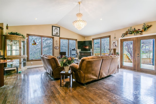 living area with a chandelier, a fireplace, vaulted ceiling, french doors, and dark wood finished floors