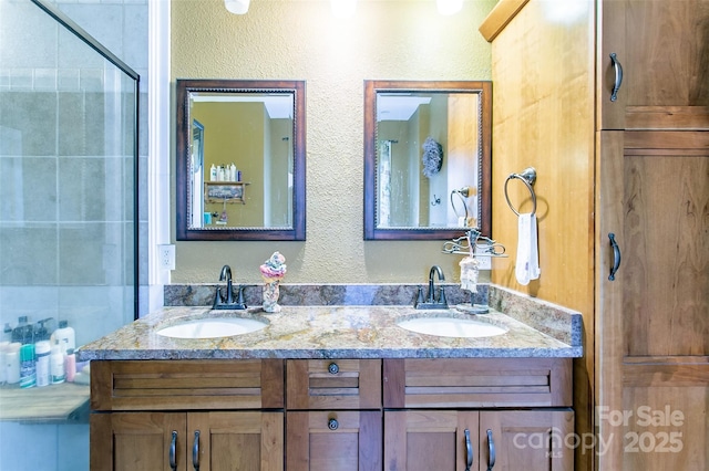 full bath featuring double vanity, tiled shower, a sink, and a textured wall