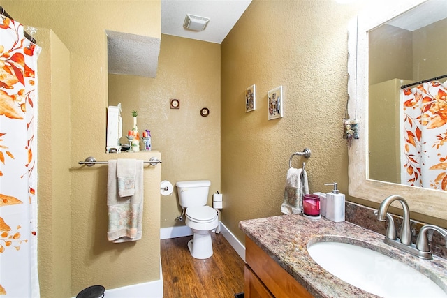 bathroom featuring visible vents, baseboards, toilet, wood finished floors, and vanity