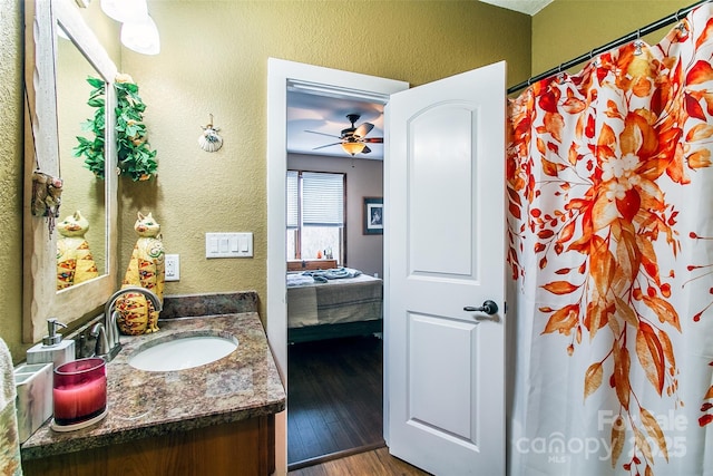 ensuite bathroom with ceiling fan, a textured wall, connected bathroom, wood finished floors, and vanity