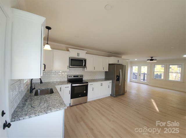 kitchen with stainless steel appliances, a sink, white cabinets, decorative backsplash, and light stone countertops