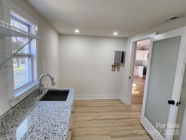 kitchen featuring light wood-style flooring, a sink, visible vents, baseboards, and light stone countertops