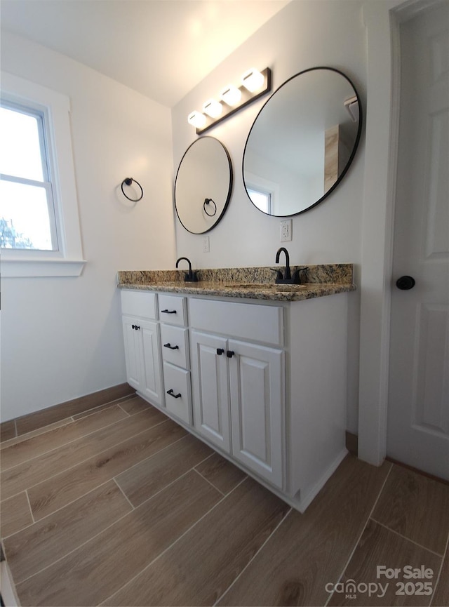 bathroom with wood tiled floor, a sink, baseboards, and double vanity