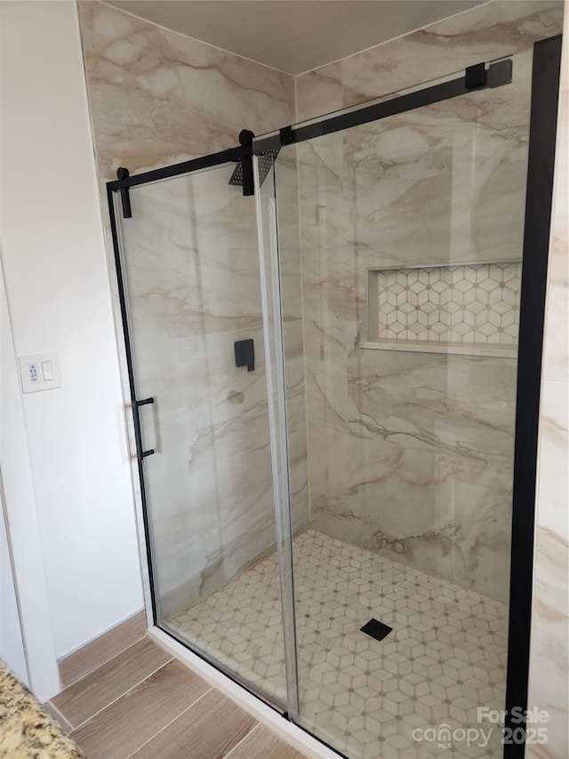 bathroom with a marble finish shower and wood finished floors