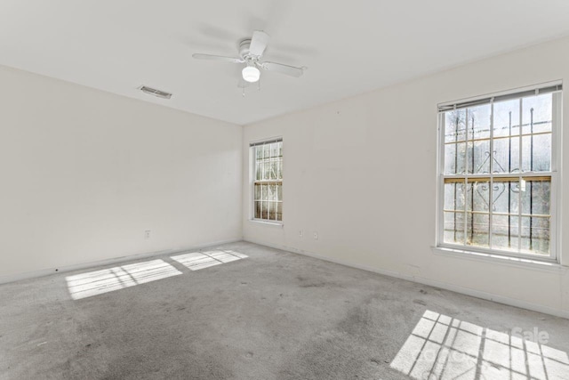 spare room with a healthy amount of sunlight, carpet floors, visible vents, and a ceiling fan