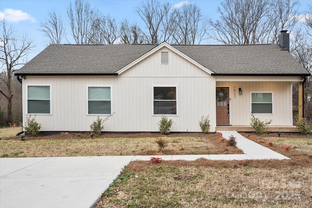 ranch-style house with a shingled roof, a chimney, and a front yard