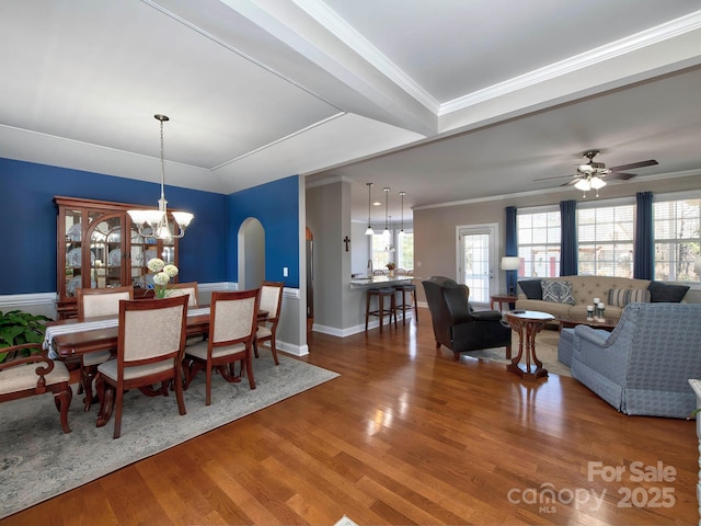 dining area with arched walkways, ornamental molding, wood finished floors, baseboards, and ceiling fan with notable chandelier