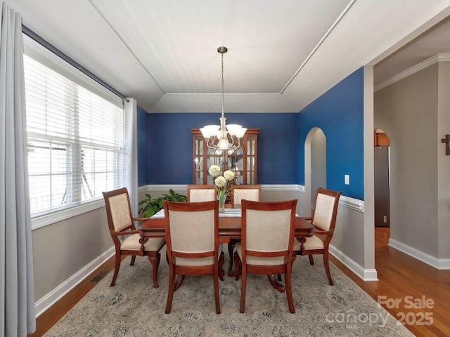 dining room featuring arched walkways, visible vents, wood finished floors, a chandelier, and baseboards