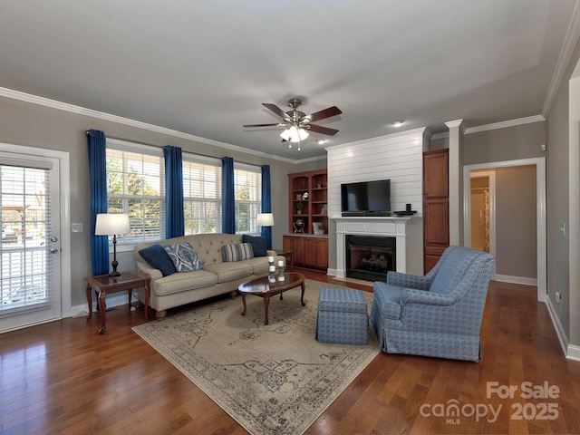 living area featuring dark wood-style floors, a fireplace, ornamental molding, and a ceiling fan