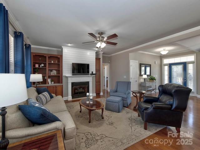 living room with a ceiling fan, a large fireplace, crown molding, and wood finished floors