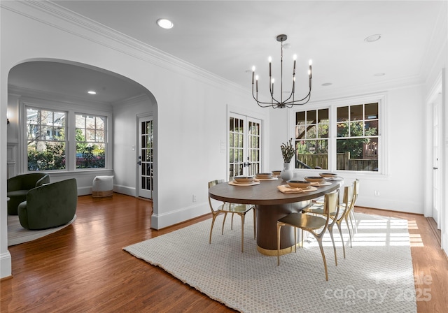 dining area with arched walkways, a notable chandelier, wood finished floors, french doors, and crown molding