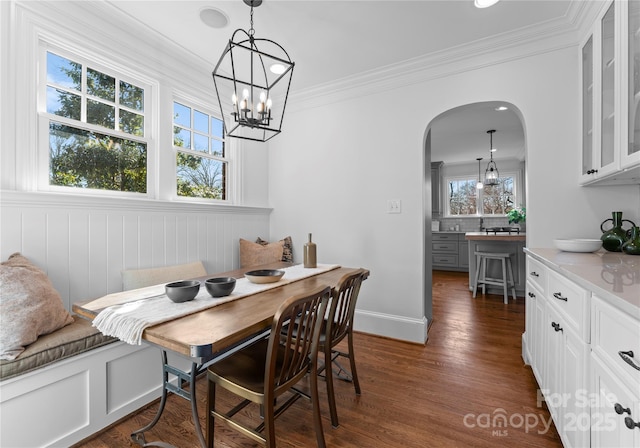 dining space with baseboards, arched walkways, dark wood-style flooring, and ornamental molding