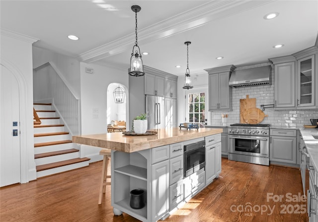 kitchen featuring premium appliances, gray cabinets, wall chimney range hood, and open shelves