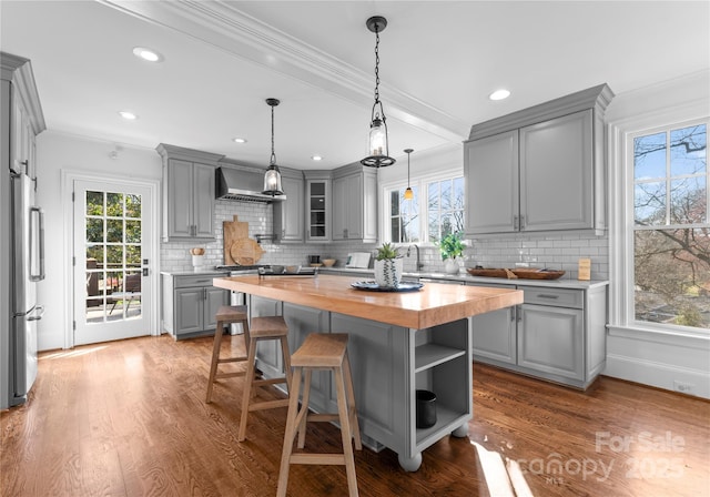 kitchen featuring butcher block countertops, light wood-style floors, gray cabinets, freestanding refrigerator, and wall chimney exhaust hood