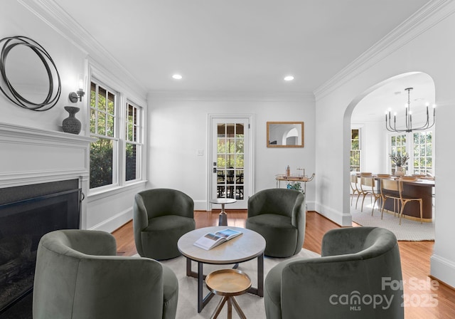 living room with arched walkways, ornamental molding, wood finished floors, and a chandelier