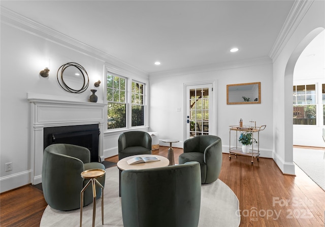 sitting room featuring arched walkways, a fireplace, wood finished floors, baseboards, and crown molding