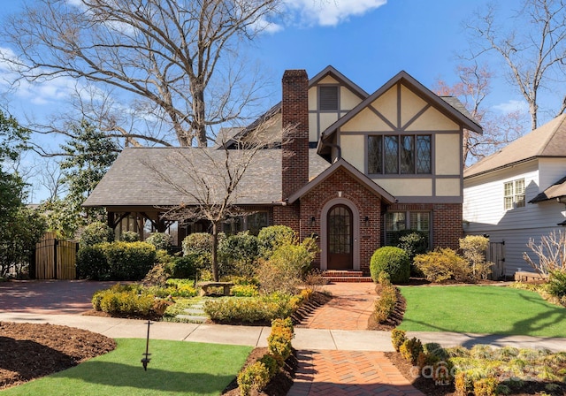 tudor home with brick siding, fence, stucco siding, a chimney, and a front yard