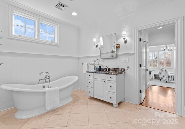 ensuite bathroom with visible vents, wainscoting, a soaking tub, ornamental molding, and tile patterned floors